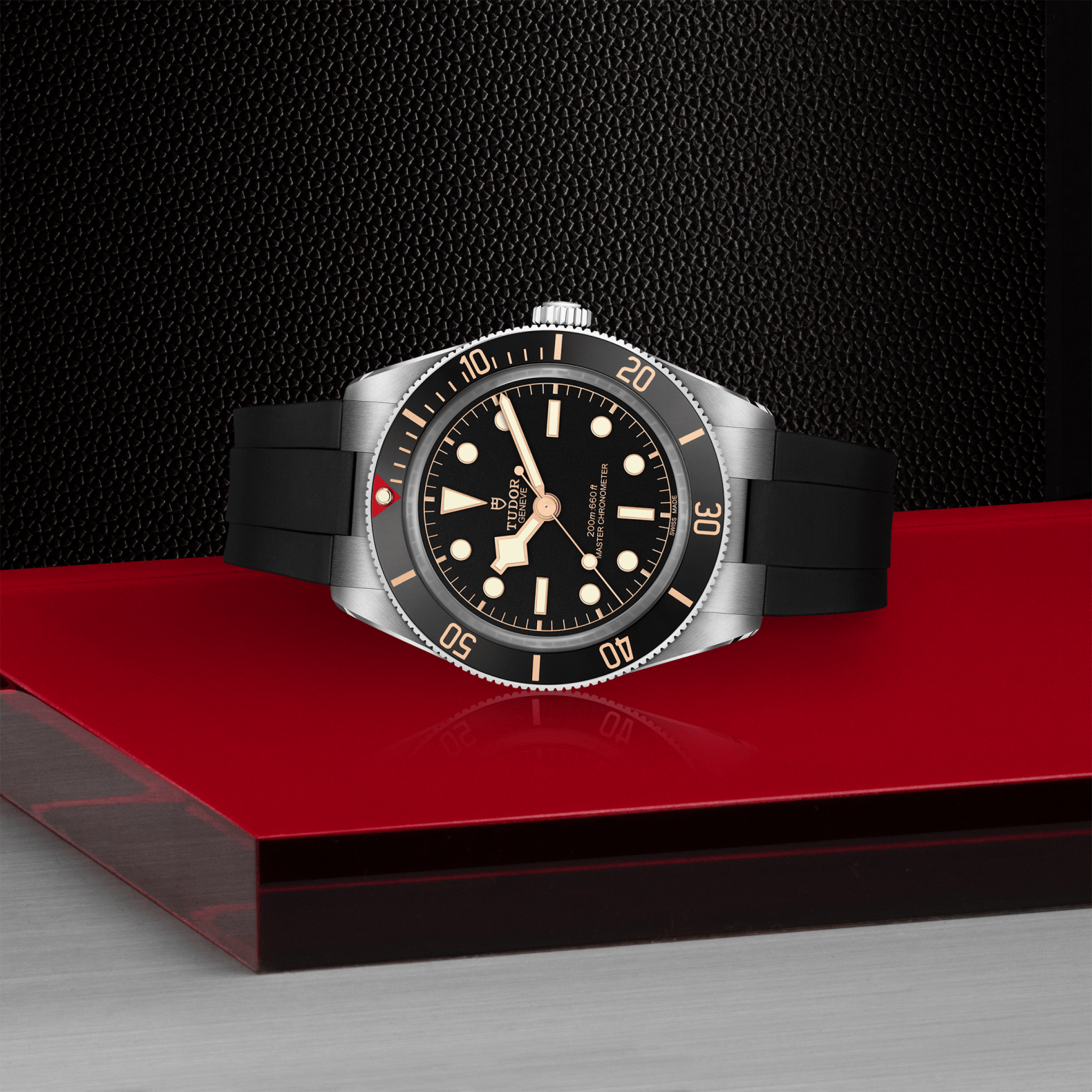 Tudor Black Bay 58 watch with a black rubber strap and black dial on red platform against a black background.