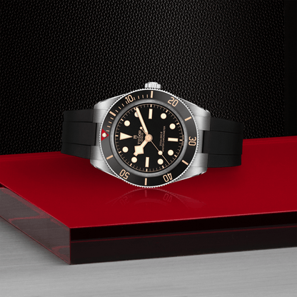 Tudor Black Bay 58 watch with a black rubber strap and black dial on red platform against a black background.