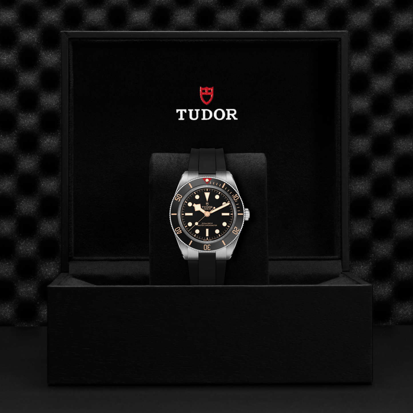 Tudor Black Bay 58 watch with a black rubber strap and black dial in a black box against a black background.