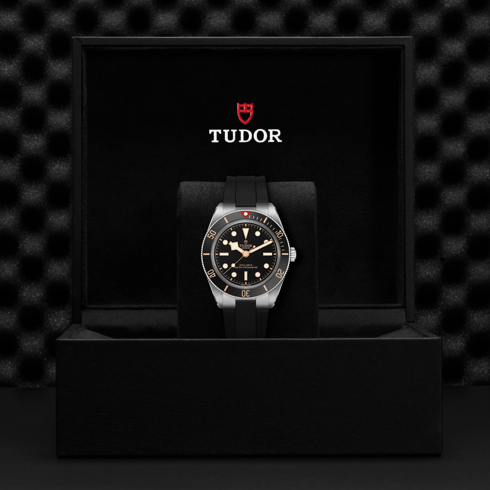 Tudor Black Bay 58 watch with a black rubber strap and black dial in a black box against a black background.