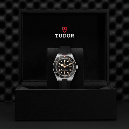Tudor Black Bay 58 watch with a black rubber strap and black dial in a black box against a black background.