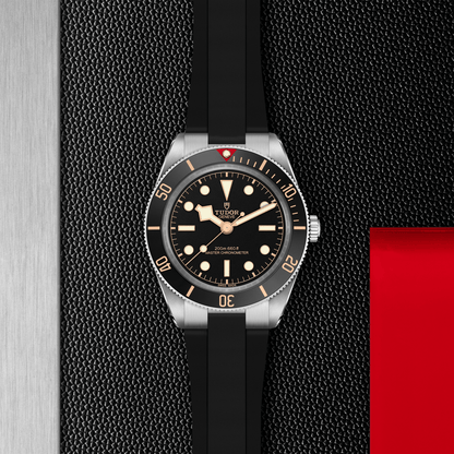 Tudor Black Bay 58 watch with a black rubber strap and black dial on a black textured background.