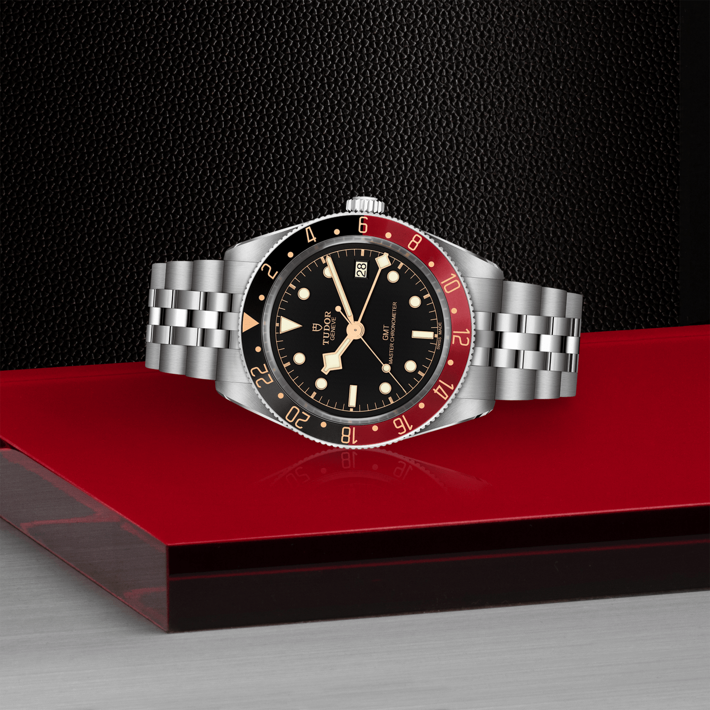 Tudor Black Bay 58 GMT watch with a steel bracelet and black dial on red platform against a black background.