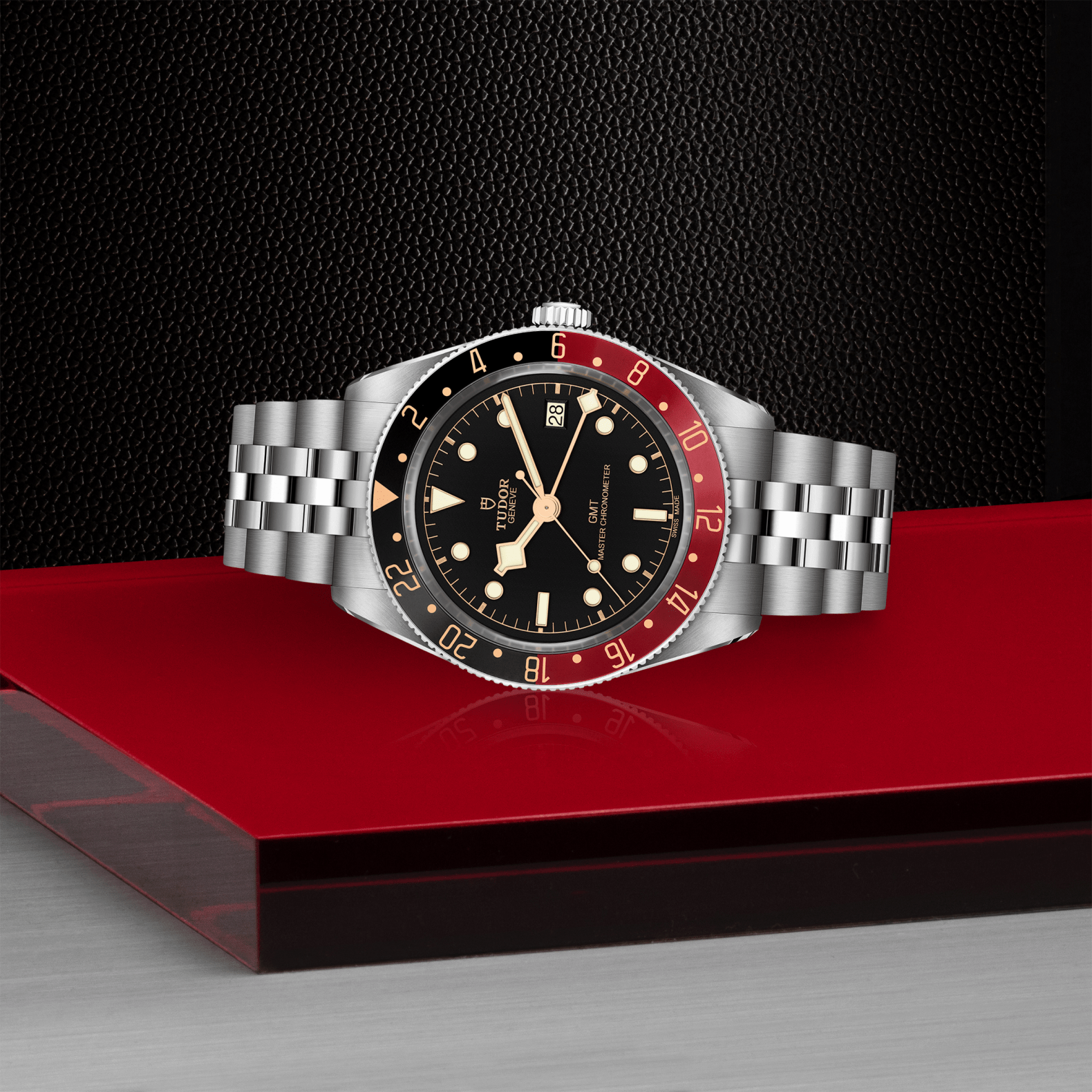 Tudor Black Bay 58 GMT watch with a steel bracelet and black dial on red platform against a black background.