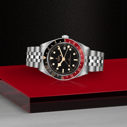 Tudor Black Bay 58 GMT watch with a steel bracelet and black dial on red platform against a black background.