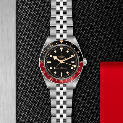 Tudor Black Bay 58 GMT watch with a steel bracelet and black dial on a black textured background.