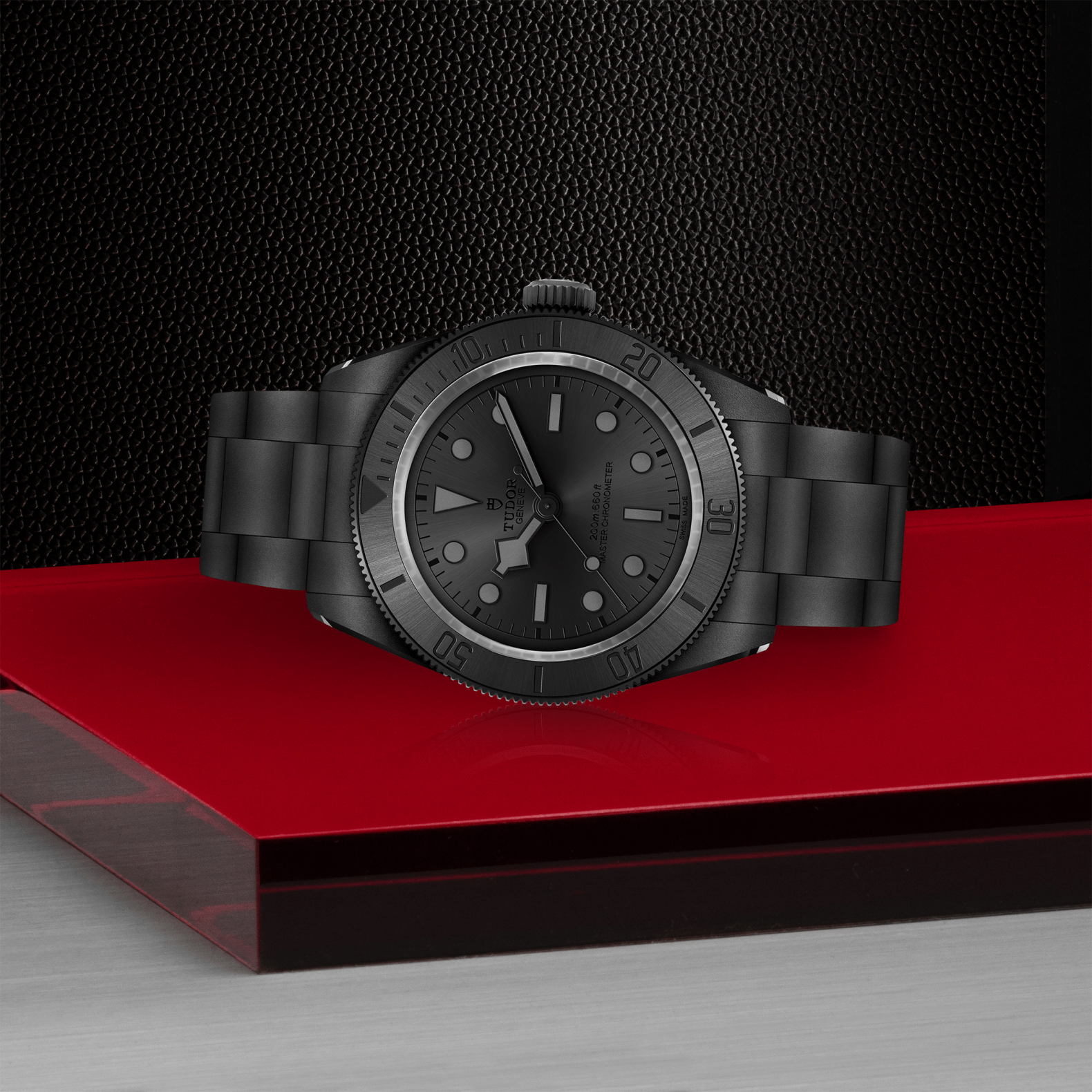 Tudor Black Bay Ceramic watch on bracelet with black dial on red platform against a black background.