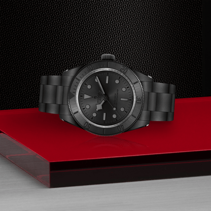 Tudor Black Bay Ceramic watch on bracelet with black dial on red platform against a black background.