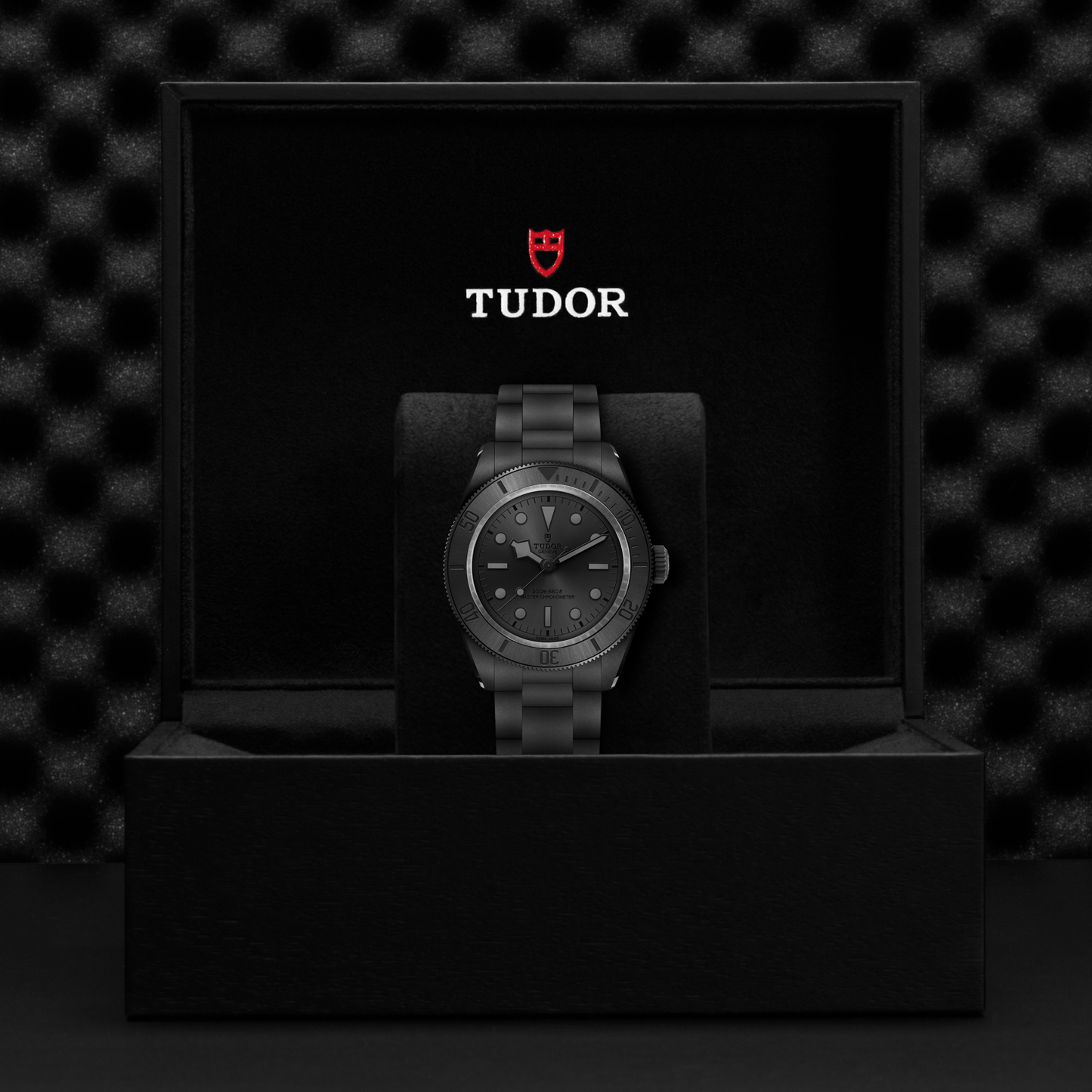 Tudor Black Bay Ceramic watch on bracelet with black dial in a black box against a black background.