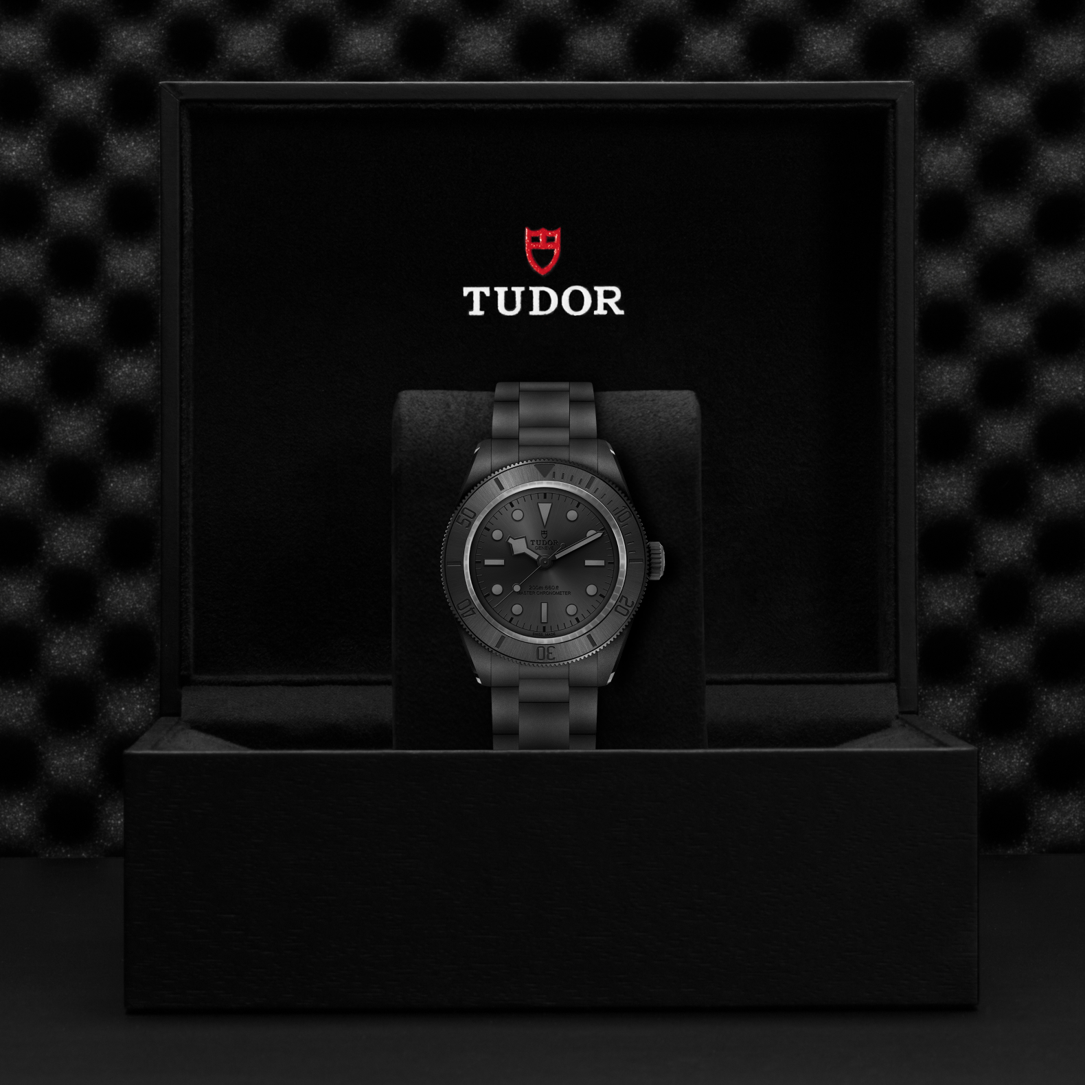 Tudor Black Bay Ceramic watch on bracelet with black dial in a black box against a black background.