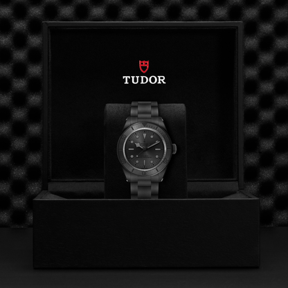 Tudor Black Bay Ceramic watch on bracelet with black dial in a black box against a black background.