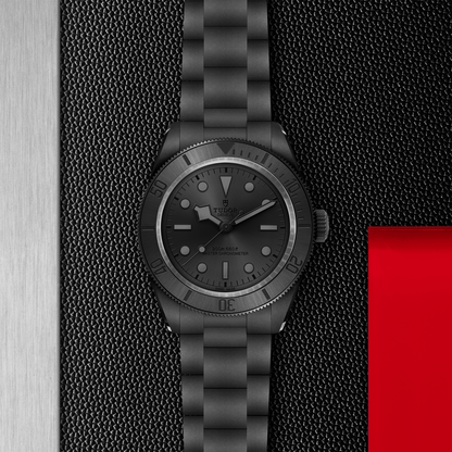 Tudor Black Bay Ceramic watch on bracelet with a black dial on a black textured background.